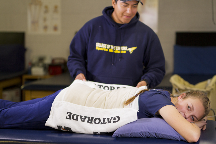 运动医学教师应用热垫在运动员的损伤后背。